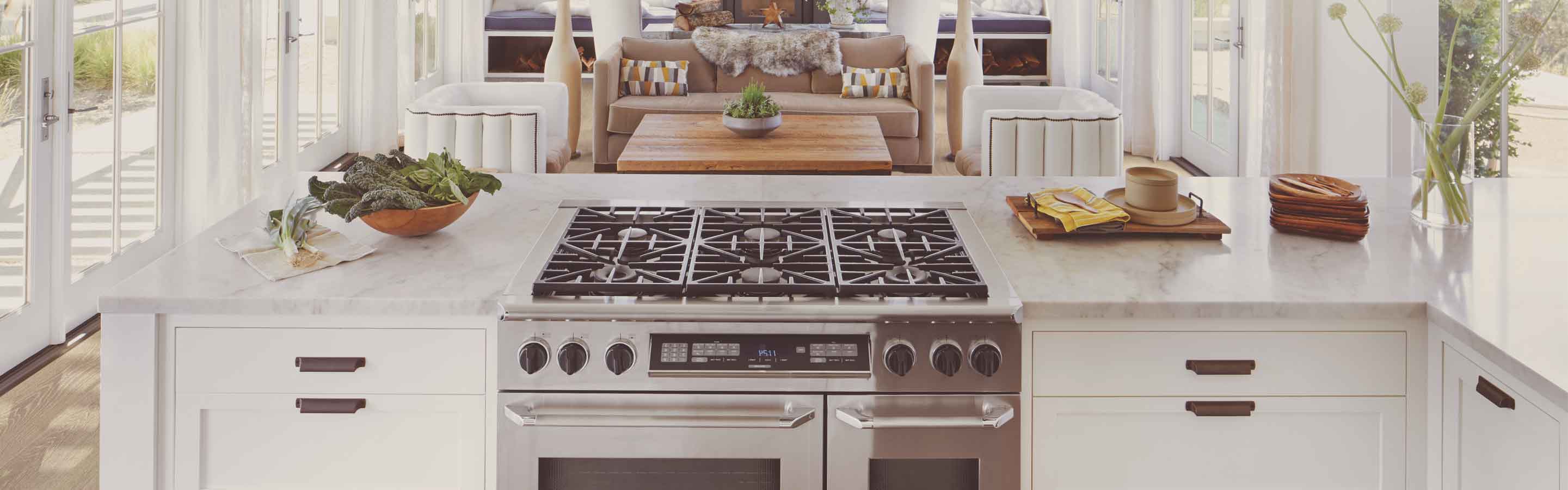 Bright kitchen with marble counter tops and white cabinets with bronze hardware.